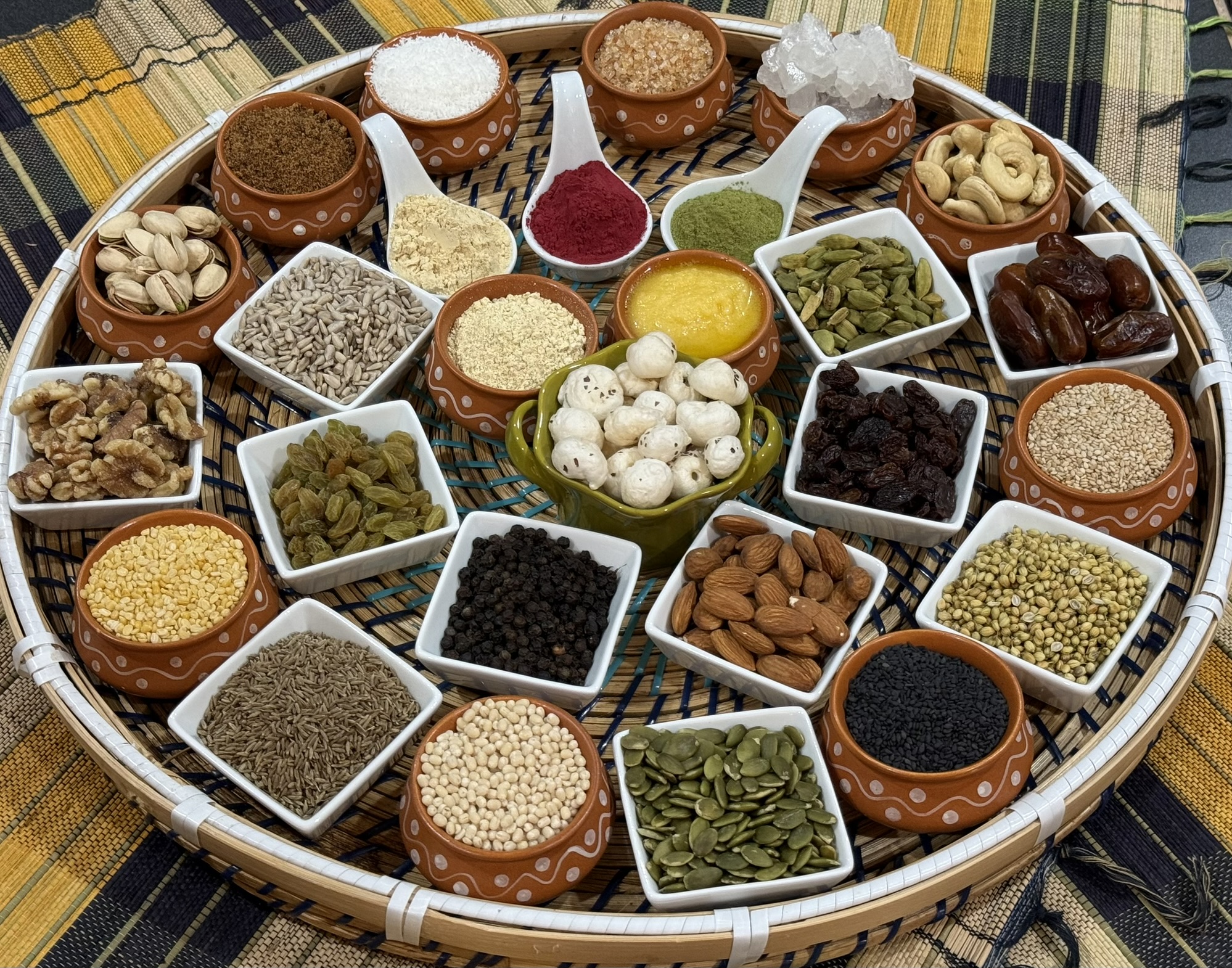 A woven tray displaying nuts, seeds, dried fruit, coconut, and spices for laddoos