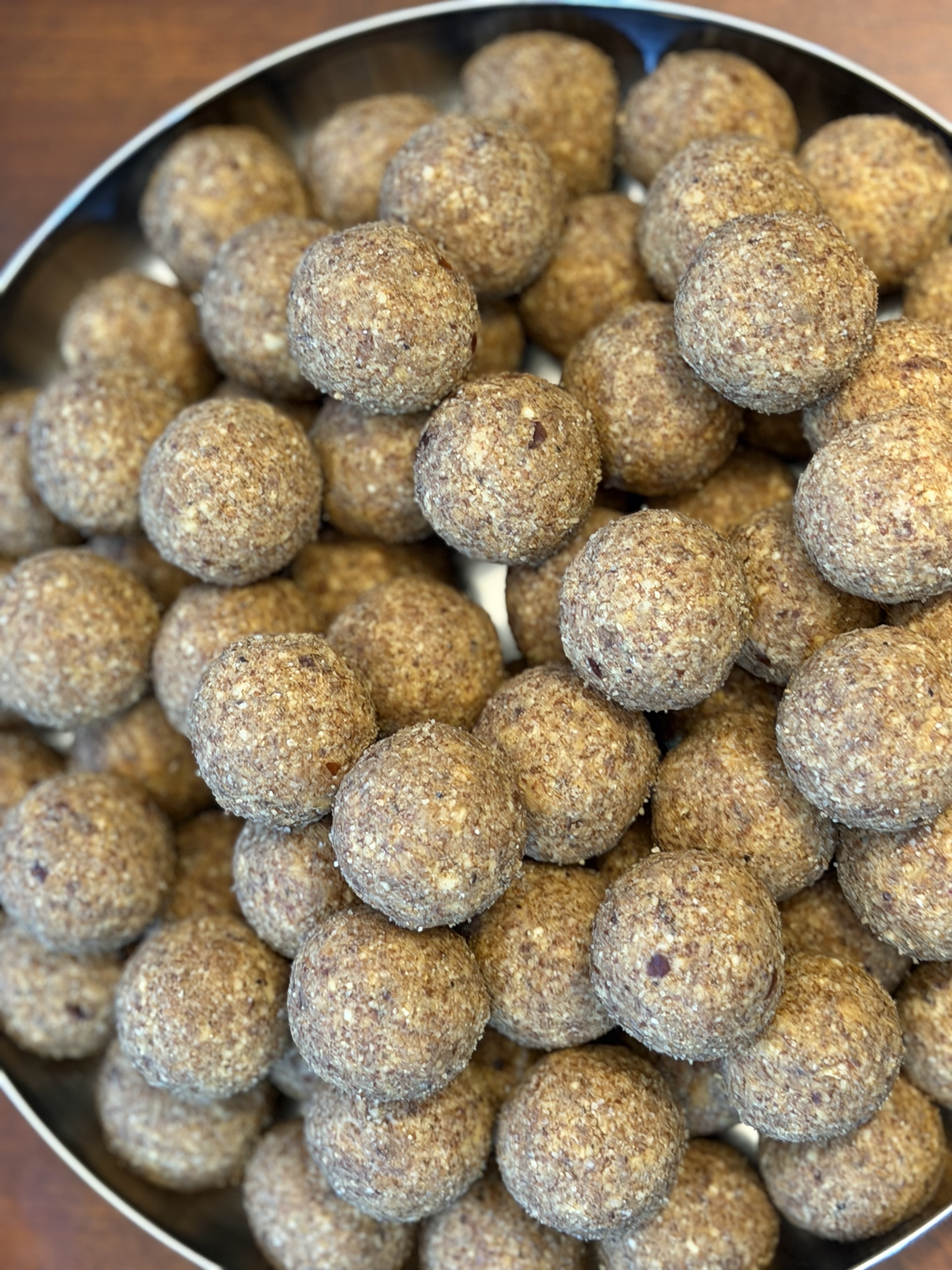 Dozens of finished laddoos filling a steel thali, fresh from one batch